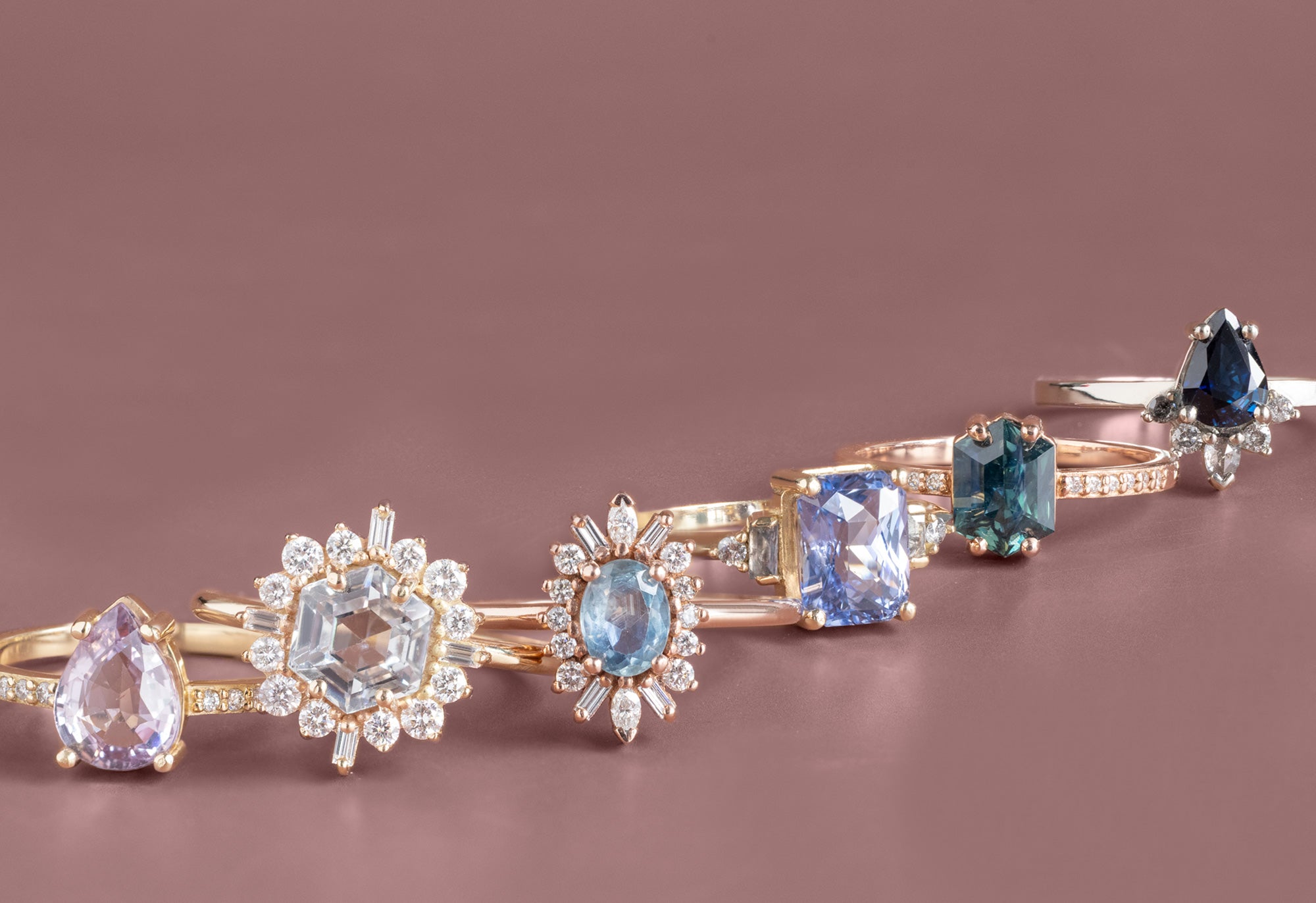 Sapphire gemstone engagement rings arranged in a line on mauve background